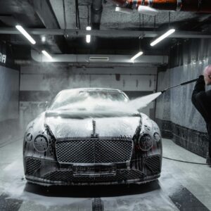 A Bentley Continental GT being washed with foam and a high-pressure hose in a car wash.