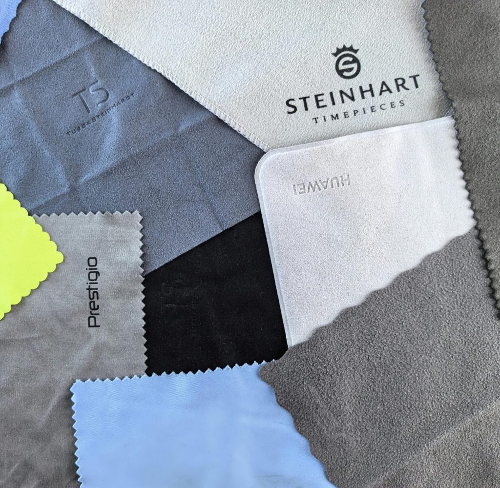 A vibrant flatlay of various cleaning cloths featuring watch brand logos on textured fabrics.